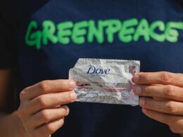 man with a greenpeache shirt holding a dove plastic sachet packaging